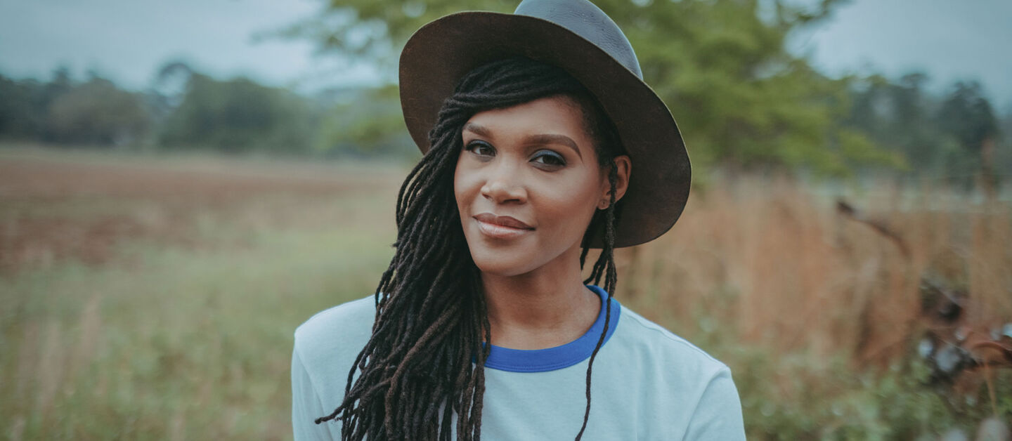 Contributing writer for this article, Candace Dantes, poses in a field wearing a gray hat.